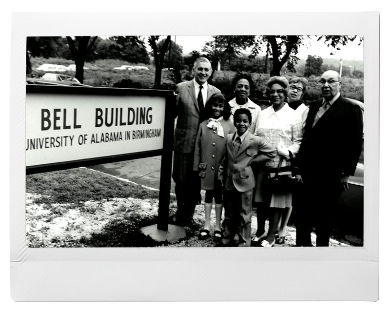 Black and white photo of Bell family with Joseph Volker next to Bell Building sign