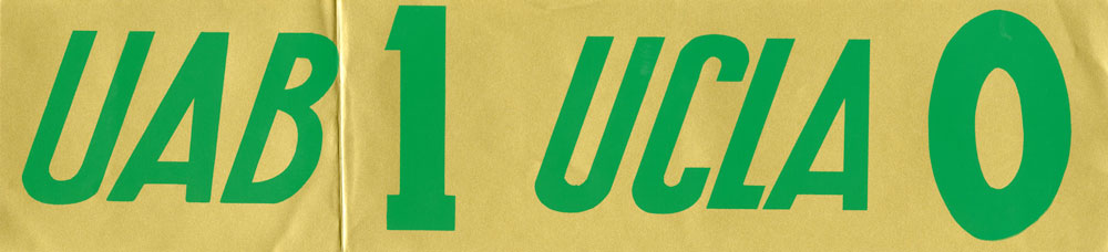 Photo of bumper sticker, with green lettering on a gold background, reading UAB 1, UCLA 0