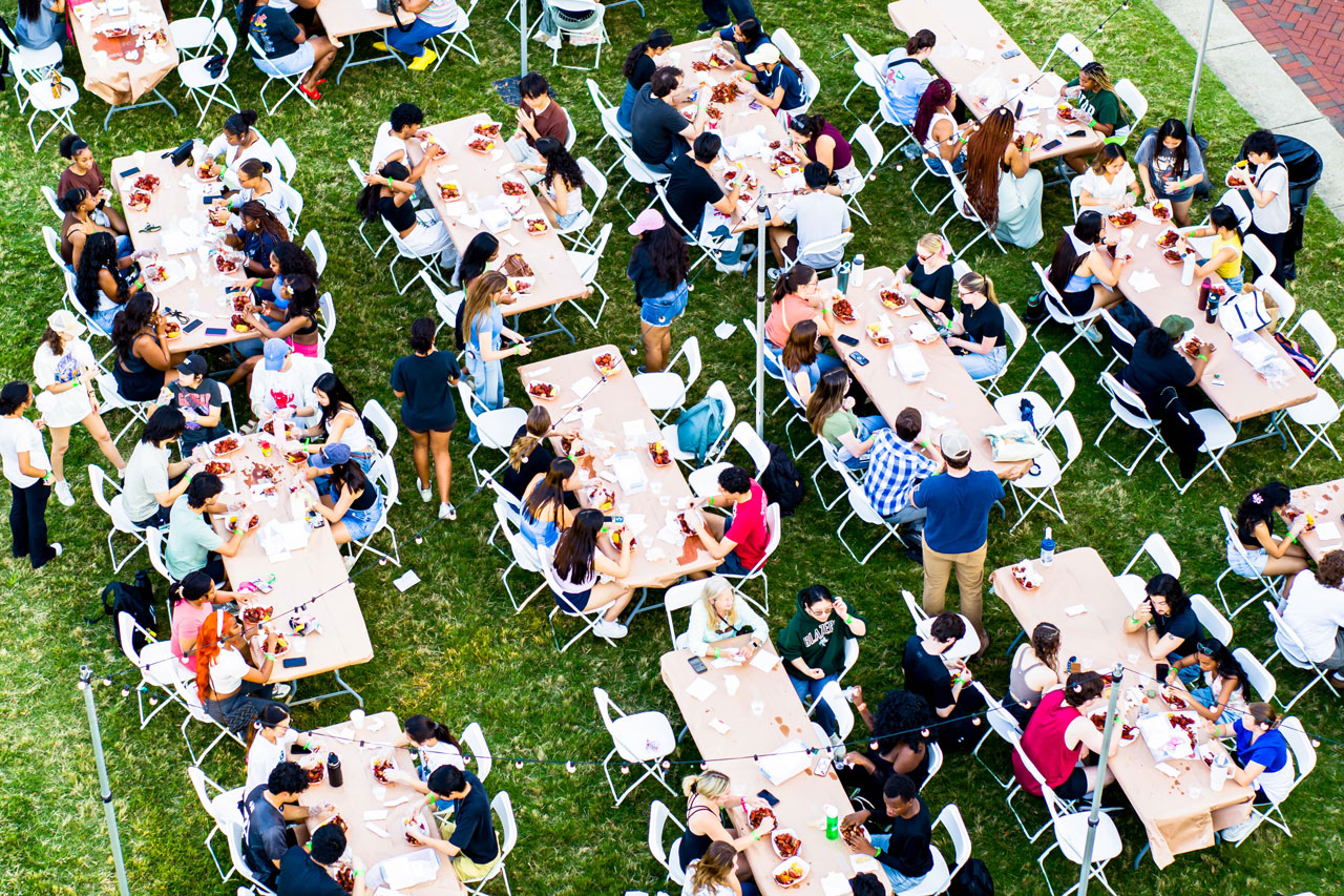 People sit at long tables during an outdoor meal on Campus Green.
