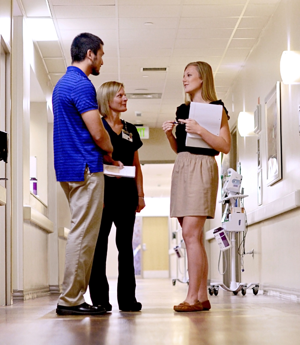 Mentor Kristen Noles (center) with Ali El-Husari (left) and Paige Severino (right) talking together in a hospital hallway.